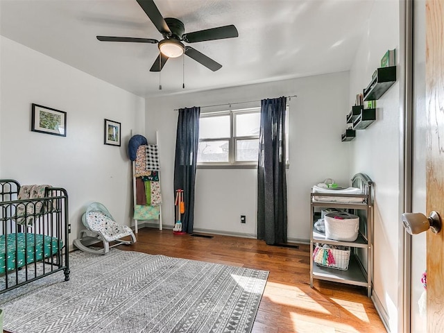 bedroom featuring a ceiling fan, visible vents, baseboards, and wood finished floors