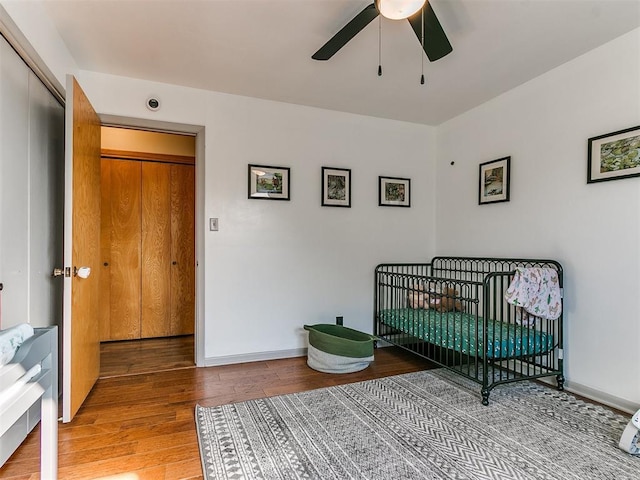 bedroom featuring a crib, ceiling fan, baseboards, and wood finished floors