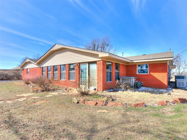 back of house featuring central air condition unit, a lawn, and brick siding