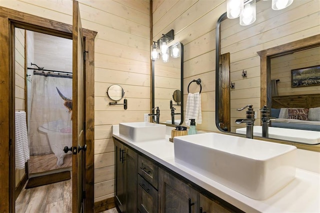 ensuite bathroom featuring double vanity, ensuite bath, wooden walls, and a sink