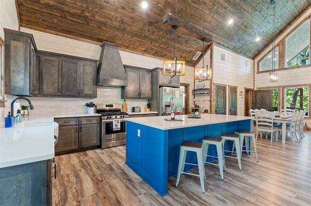 kitchen with a center island, stainless steel appliances, light countertops, dark brown cabinets, and wall chimney exhaust hood