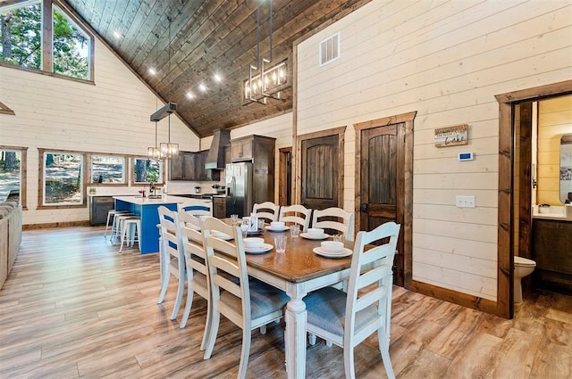 dining room featuring high vaulted ceiling, a chandelier, wood walls, and light wood-style flooring