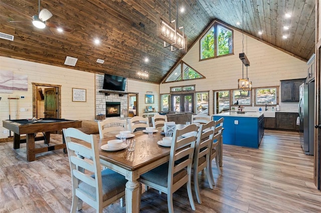 dining area featuring high vaulted ceiling, plenty of natural light, a fireplace, and light wood-style floors