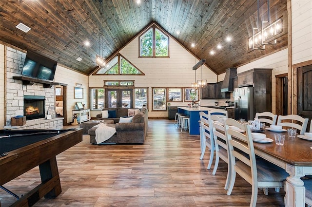 dining area with high vaulted ceiling, light wood-type flooring, a fireplace, and wood walls