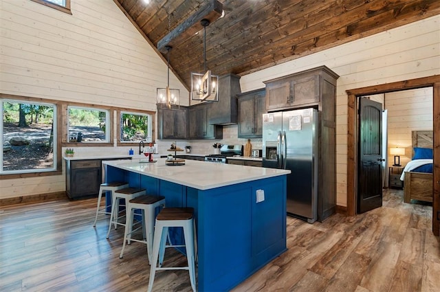 kitchen with decorative light fixtures, stainless steel appliances, light countertops, a kitchen island, and dark brown cabinets