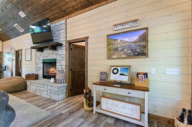 living area with a stone fireplace, wood finished floors, and wooden walls