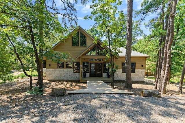 rustic home featuring stone siding, french doors, and metal roof