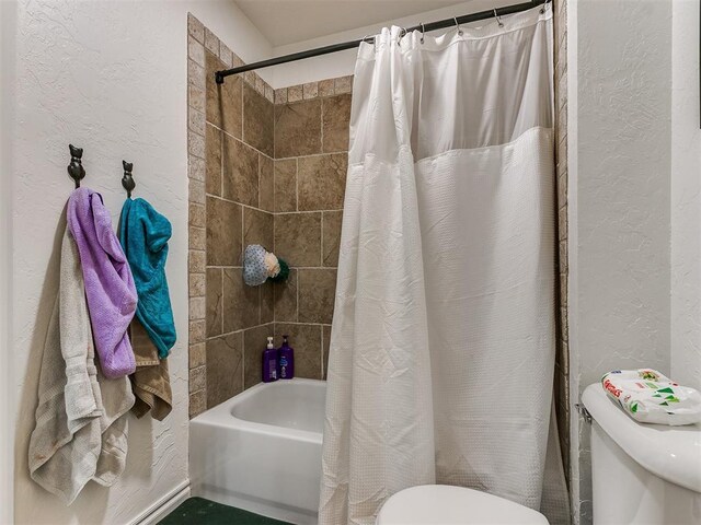 full bath featuring shower / bath combination with curtain, a textured wall, and toilet