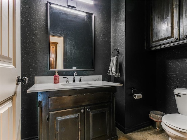 half bathroom featuring a textured wall, vanity, and toilet