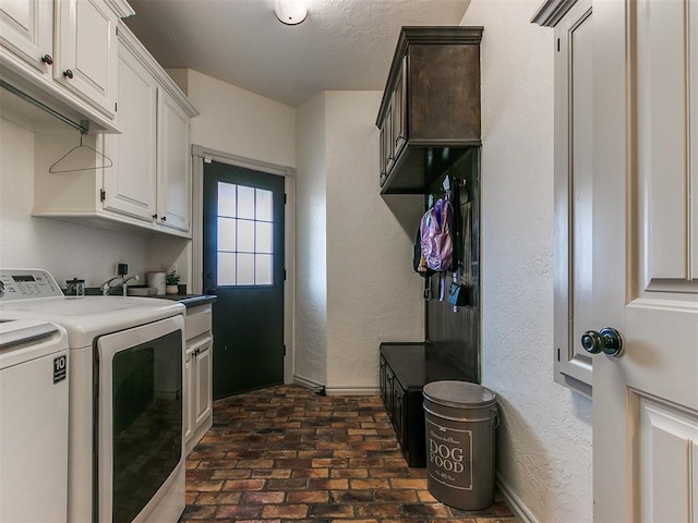 laundry room featuring a textured wall, washer and clothes dryer, brick floor, and cabinet space