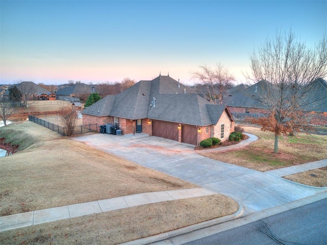 view of front of house featuring an attached garage, brick siding, fence, a yard, and driveway