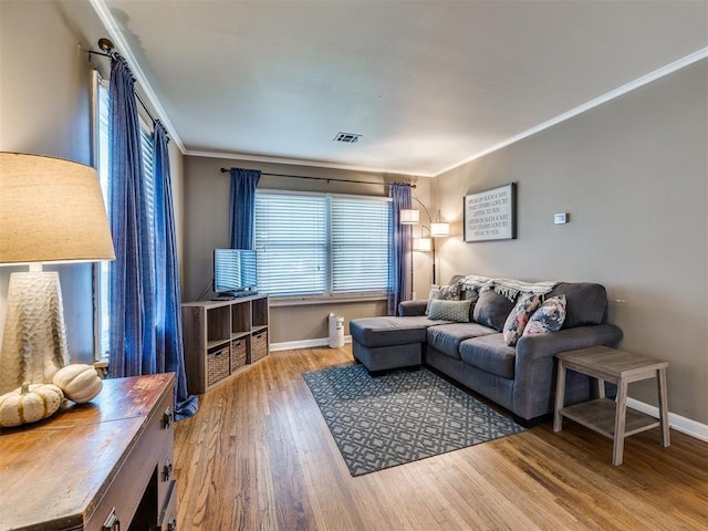 living room with ornamental molding, visible vents, baseboards, and wood finished floors