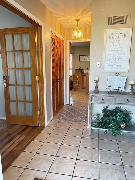 hallway featuring light tile patterned floors, visible vents, and a notable chandelier