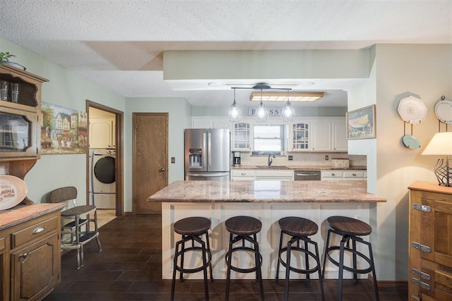 kitchen with a breakfast bar area, appliances with stainless steel finishes, stacked washer / dryer, glass insert cabinets, and white cabinets