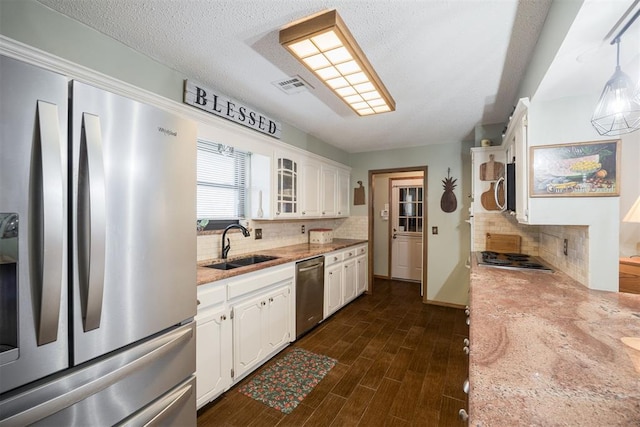 kitchen featuring appliances with stainless steel finishes, pendant lighting, white cabinetry, and glass insert cabinets