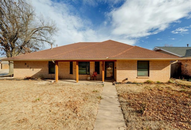 ranch-style house featuring a patio, brick siding, and roof with shingles