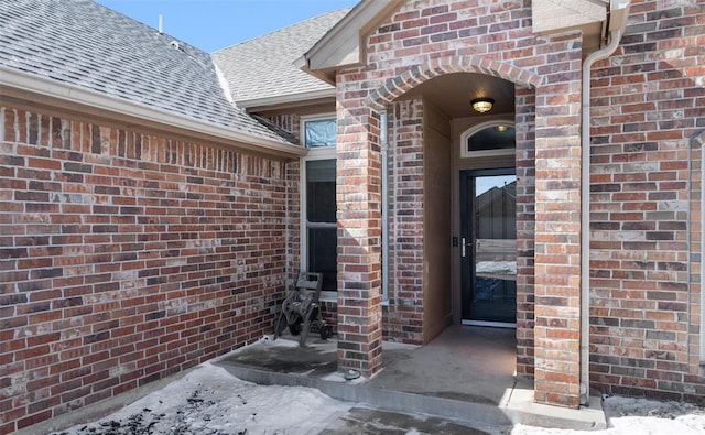 property entrance featuring a shingled roof and brick siding