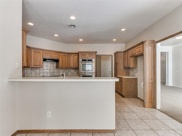 kitchen featuring stainless steel double oven, light countertops, under cabinet range hood, and a peninsula