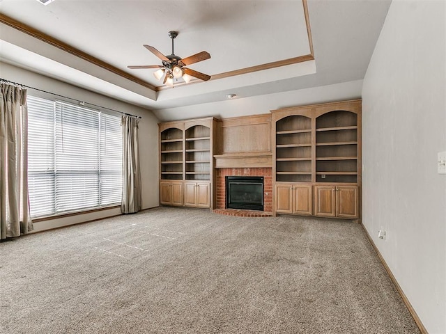 unfurnished living room with light carpet, a tray ceiling, a brick fireplace, and crown molding