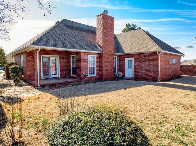 back of property featuring brick siding, a patio, a chimney, a shingled roof, and a lawn