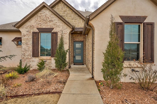 doorway to property featuring stone siding, stucco siding, and brick siding