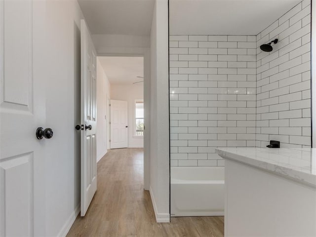 bathroom featuring wood finished floors, bathing tub / shower combination, and baseboards