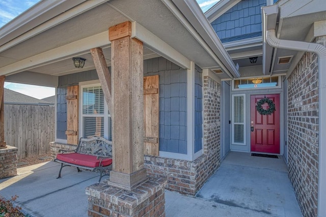 view of exterior entry featuring brick siding and fence