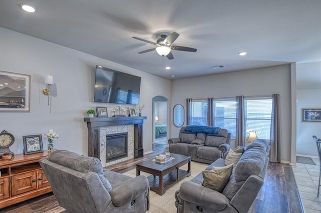 living room with arched walkways, ceiling fan, a premium fireplace, and wood finished floors