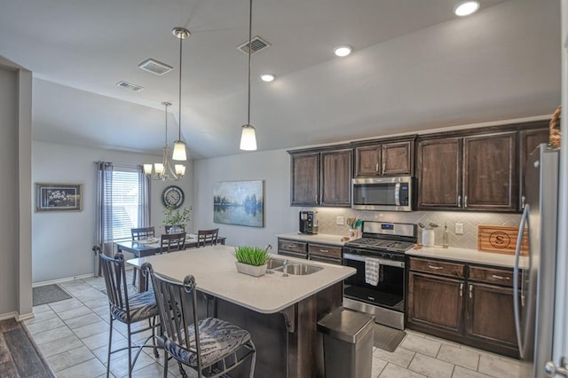 kitchen featuring a kitchen breakfast bar, hanging light fixtures, a kitchen island with sink, stainless steel appliances, and light countertops