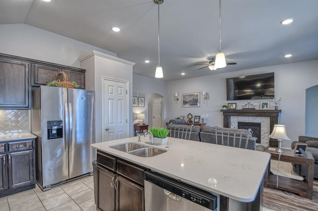 kitchen featuring arched walkways, stainless steel appliances, open floor plan, a kitchen island with sink, and a sink