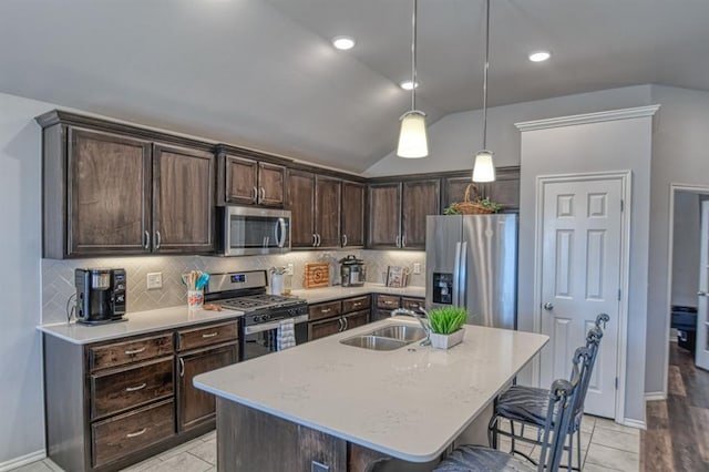 kitchen with a center island with sink, hanging light fixtures, stainless steel appliances, a kitchen bar, and a sink