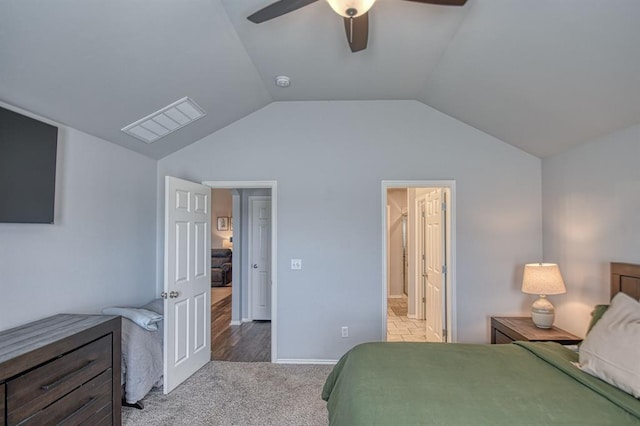 bedroom featuring lofted ceiling, ensuite bathroom, light colored carpet, visible vents, and a ceiling fan