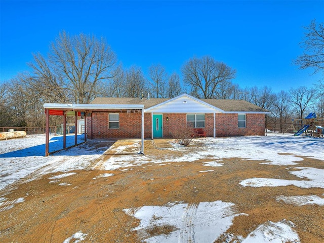 snow covered back of property with driveway, brick siding, and a playground