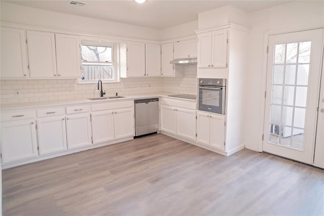 kitchen featuring decorative backsplash, white cabinets, appliances with stainless steel finishes, under cabinet range hood, and a sink