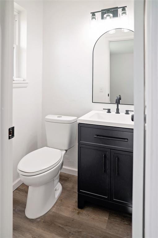 half bathroom with vanity, wood finished floors, toilet, and baseboards