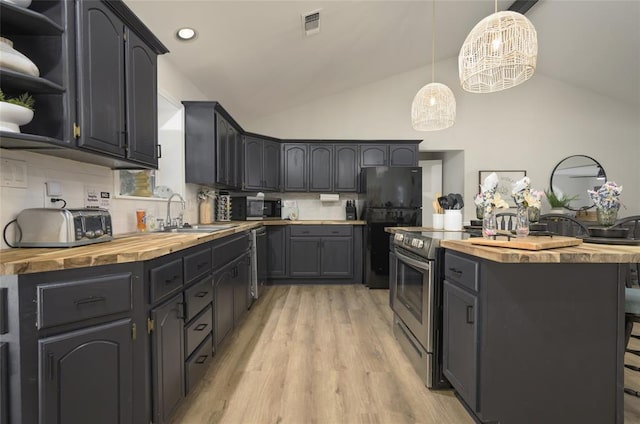 kitchen featuring butcher block countertops, vaulted ceiling, a sink, and appliances with stainless steel finishes