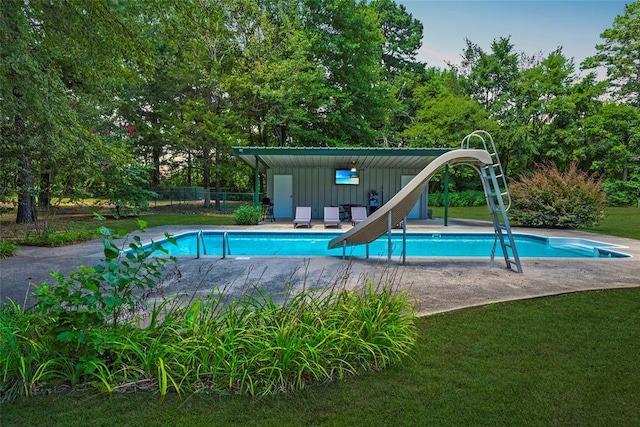 pool with a patio, a water slide, a lawn, and fence