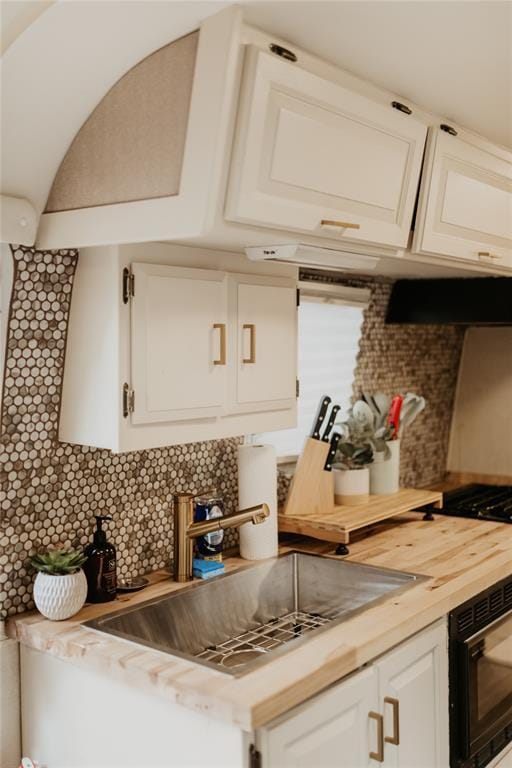 kitchen with white cabinets, a sink, decorative backsplash, and wooden counters