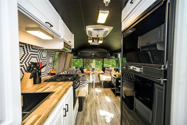 kitchen featuring wooden counters, gas range oven, white cabinetry, and light wood-style floors