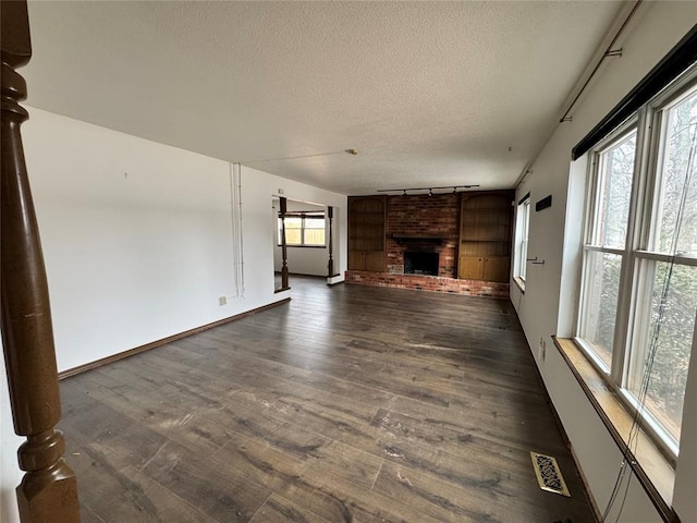 unfurnished living room with a textured ceiling, dark wood-type flooring, a fireplace, baseboards, and rail lighting