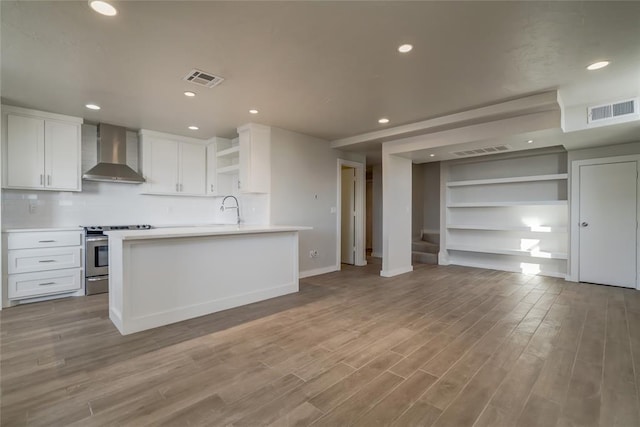 kitchen with visible vents, light countertops, stainless steel range with electric cooktop, wall chimney range hood, and white cabinetry