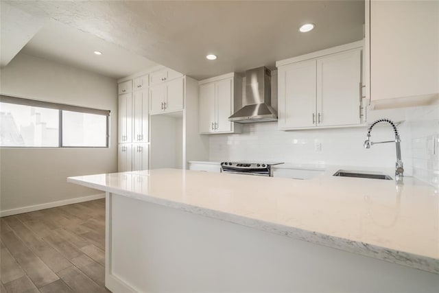 kitchen with wall chimney exhaust hood, a peninsula, stainless steel electric range, white cabinetry, and a sink