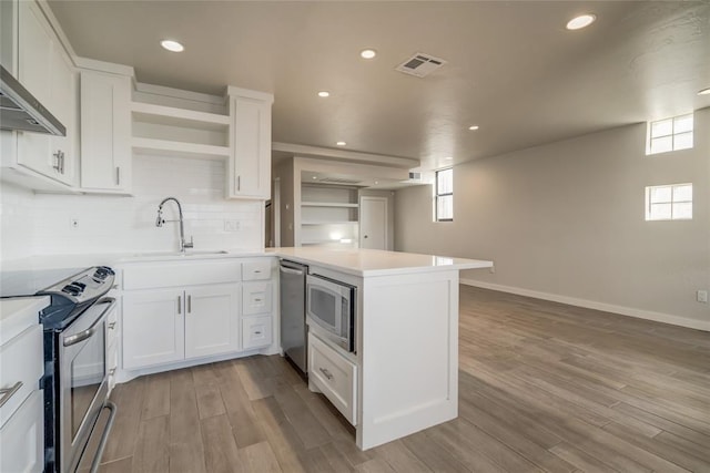 kitchen with a peninsula, stainless steel appliances, a sink, light countertops, and open shelves