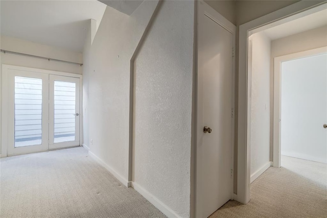 hall with baseboards, a textured wall, and light colored carpet