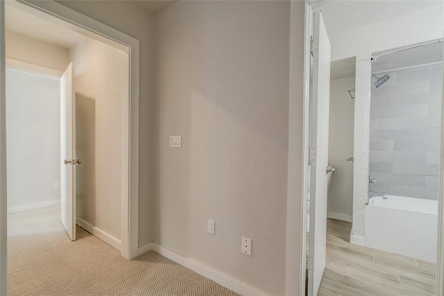 hallway featuring light colored carpet and baseboards