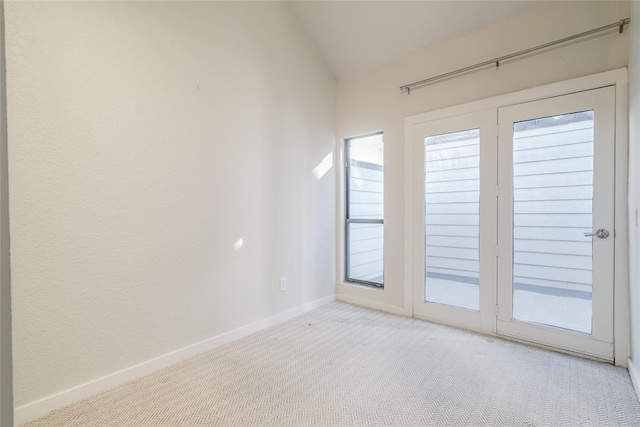 spare room featuring light colored carpet, vaulted ceiling, and baseboards