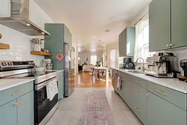 kitchen with wall chimney range hood, appliances with stainless steel finishes, light countertops, and a sink