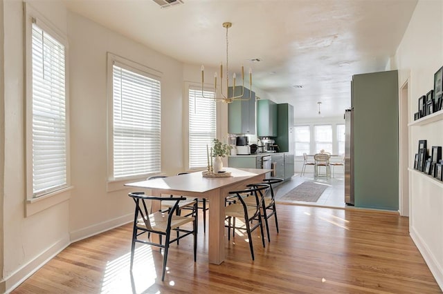 dining area featuring light wood finished floors, visible vents, baseboards, and an inviting chandelier