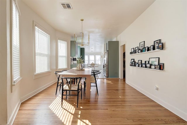 dining area featuring light wood-type flooring, an inviting chandelier, baseboards, and visible vents