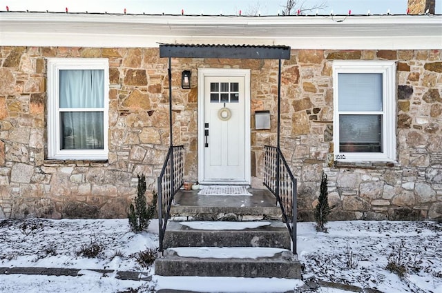 snow covered property entrance with stone siding